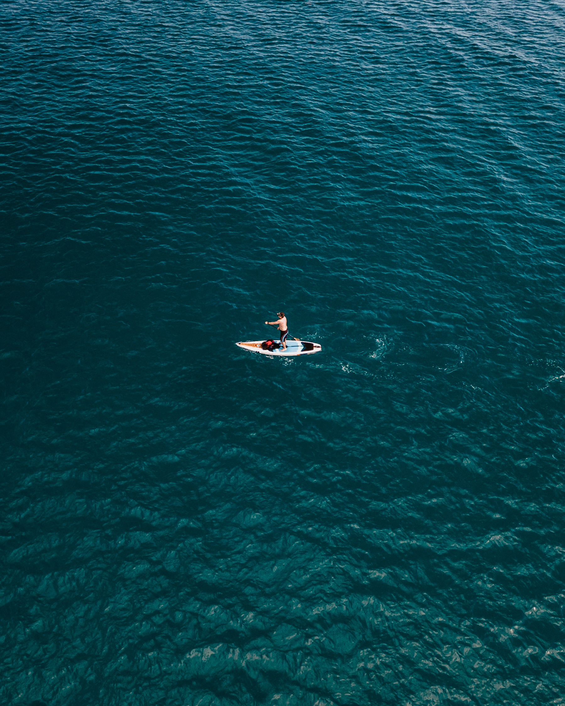 A paddleboarder crossing deep blue water from above