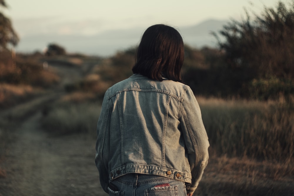 woman in brown jacket and blue denim jeans standing on dirt road during daytime