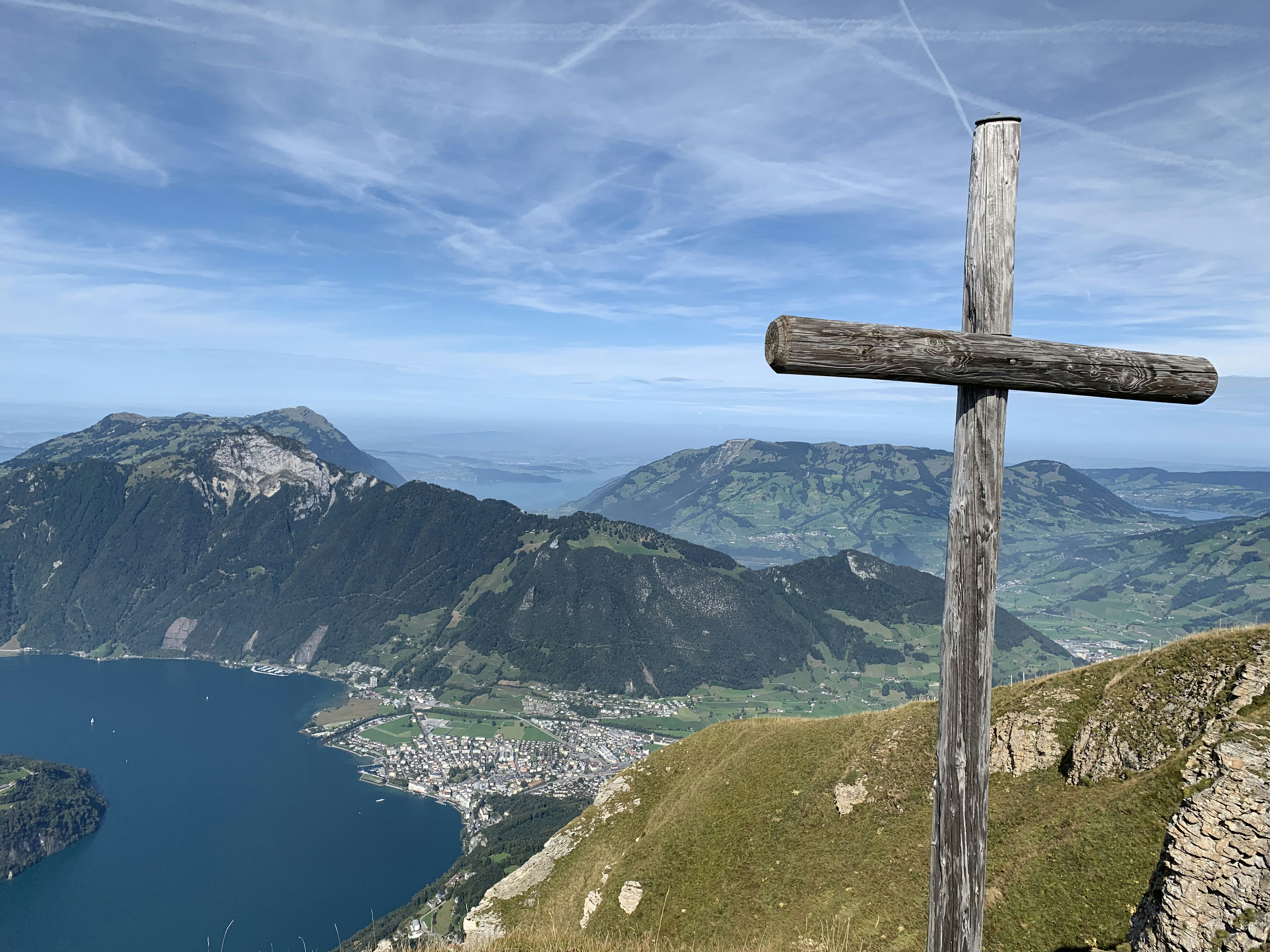 brown wooden cross on green grass field near lake and mountains during daytime