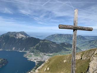 brown wooden cross on green grass field near lake and mountains during daytime