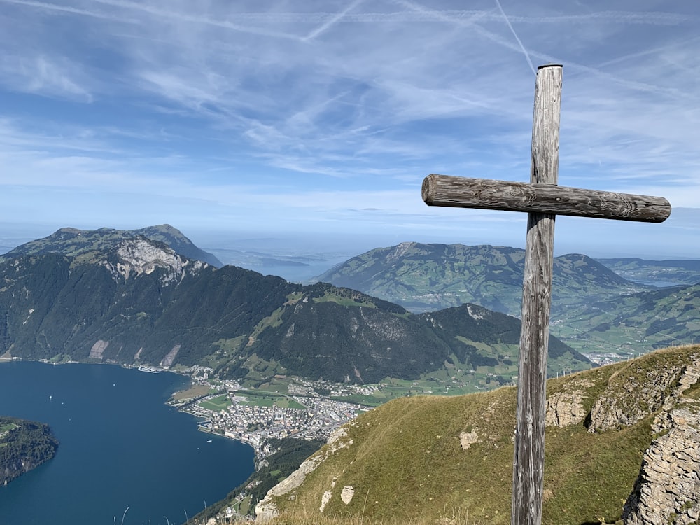 cruz de madeira marrom no campo de grama verde perto do lago e das montanhas durante o dia