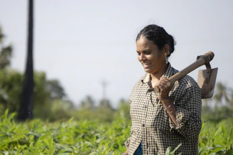 A close-up shot of an African female farmer holding a digital tablet in a lush green field, with sunlight filtering through nearby trees.