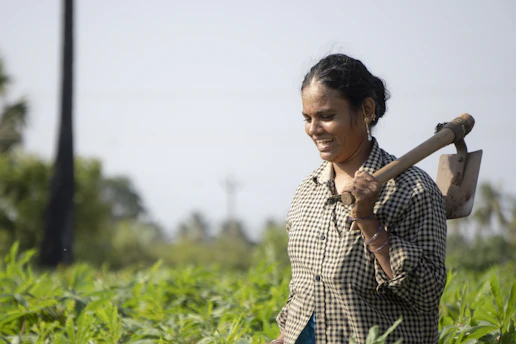 A close-up shot of an African female farmer holding a digital tablet in a lush green field, with sunlight filtering through nearby trees.