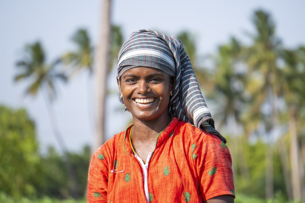 smiling woman in orange button up shirt wearing gray and white striped knit cap