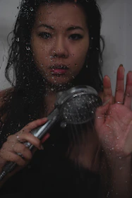 Hands installing a water-saving shower aerator under a modern bathroom showerhead.