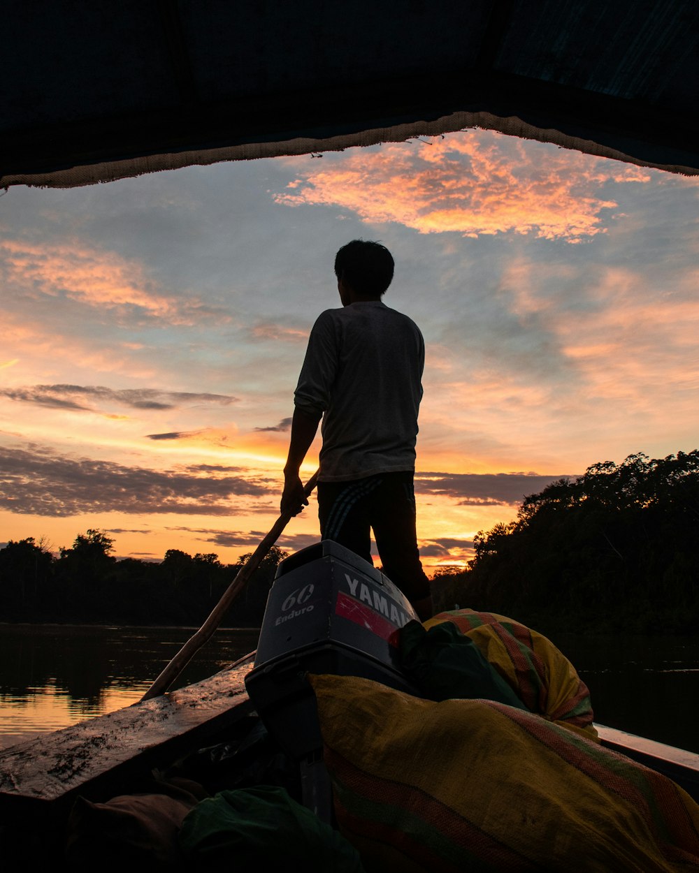 man in white shirt and black shorts standing on brown wooden boat during sunset