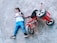 A child is lying on the pavement next to a fallen red tricycle. The child appears to be wearing a white shirt and blue pants.
