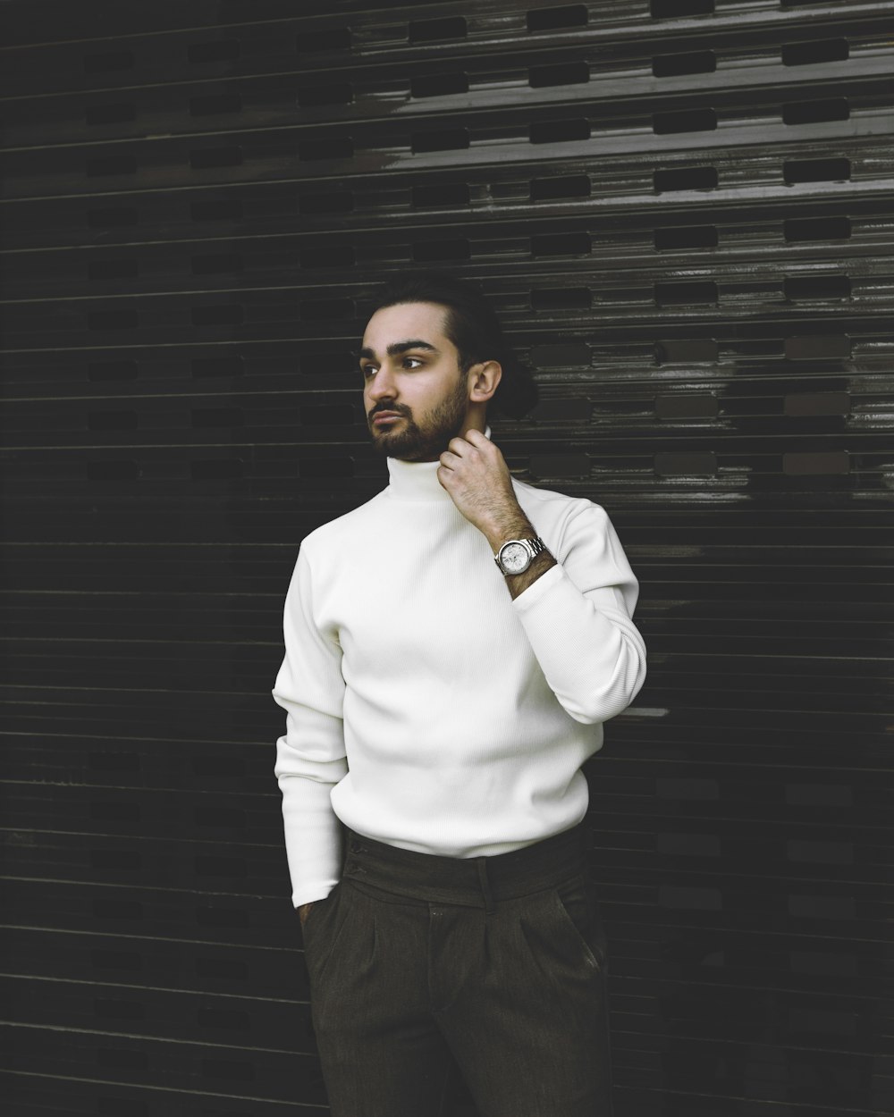 man in white dress shirt and black pants standing beside black wall