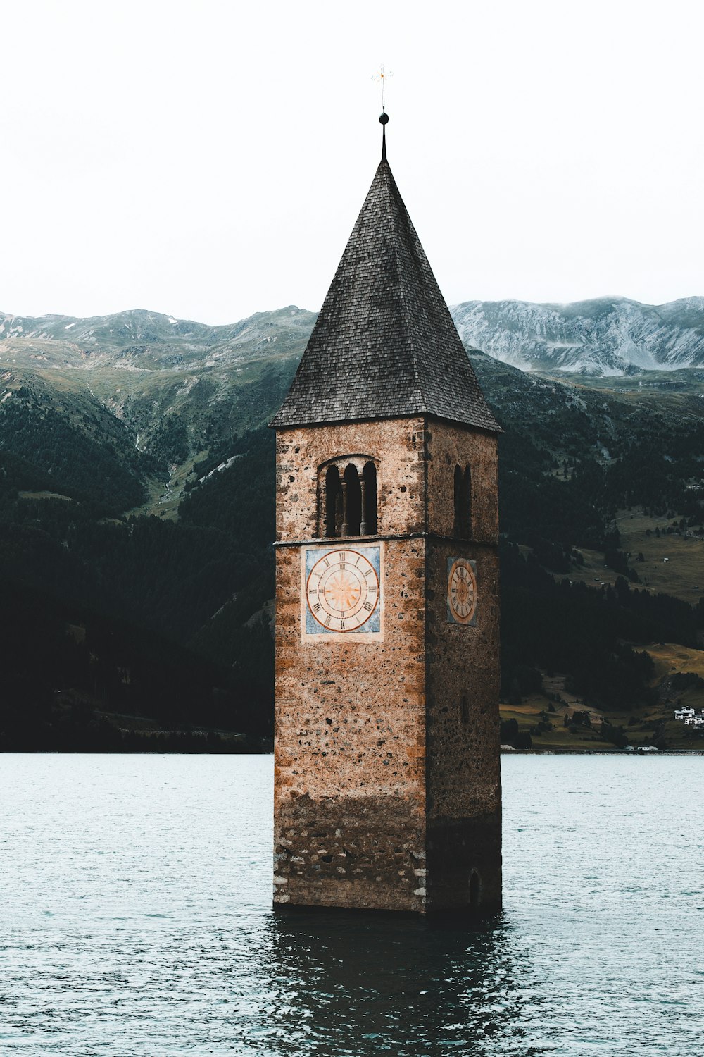 brown brick tower near lake and snow covered mountain