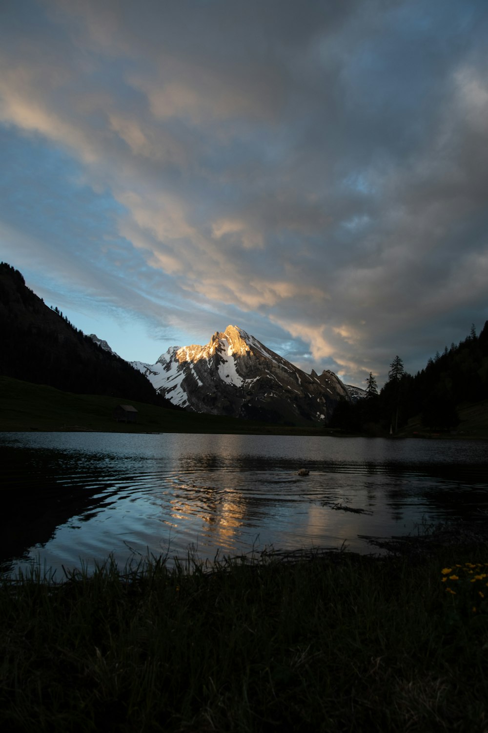 body of water near mountain under cloudy sky during daytime