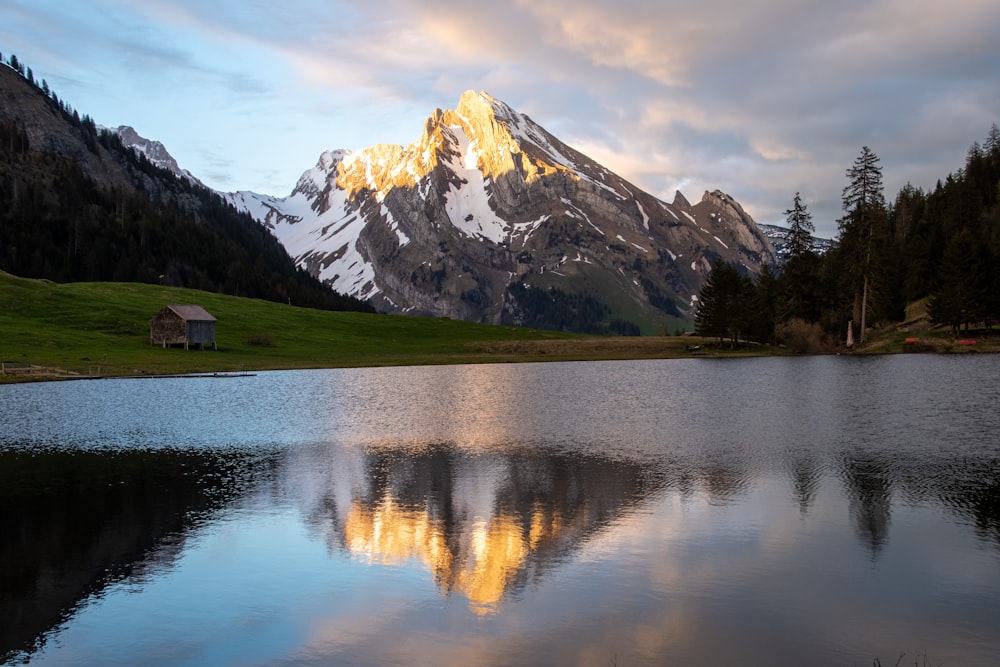 lake near green grass and trees and snow covered mountain during daytime