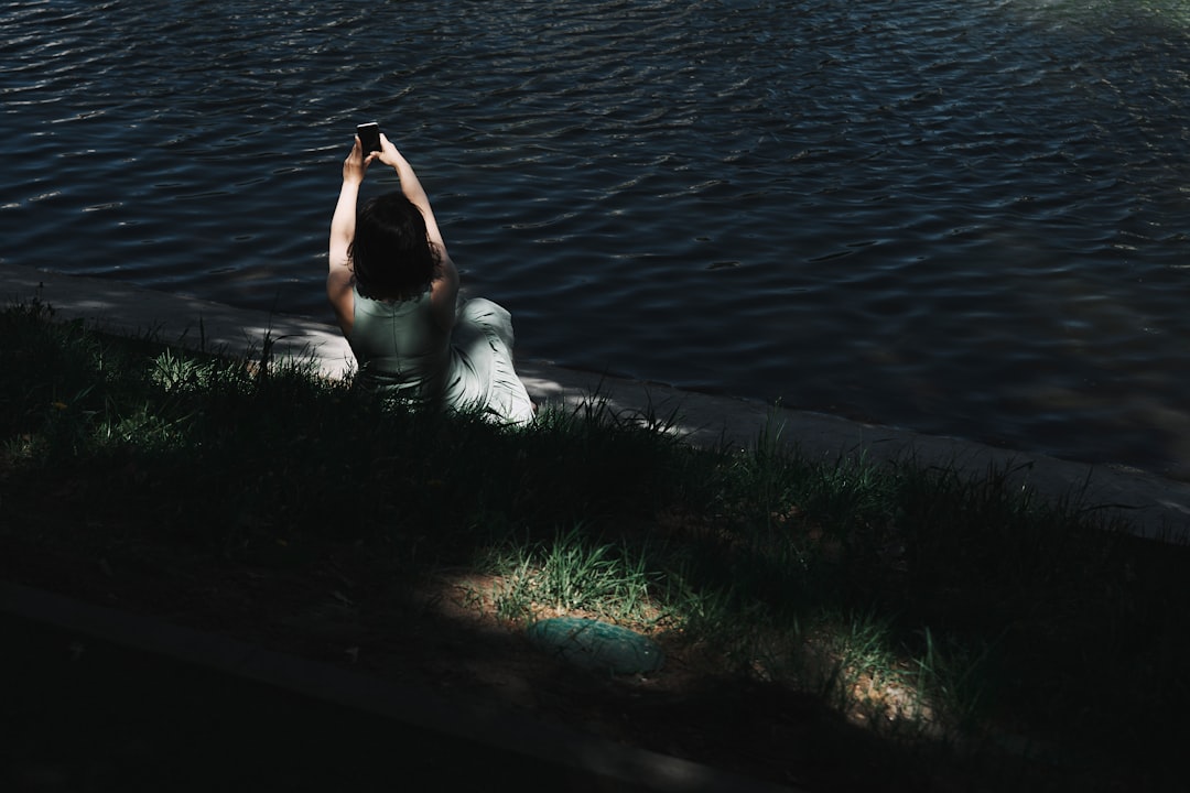 woman in white dress lying on green grass near body of water during daytime