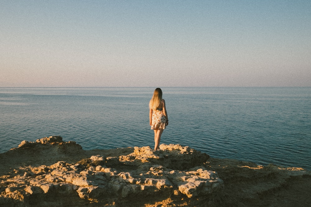 woman in brown dress standing on rocky shore during daytime