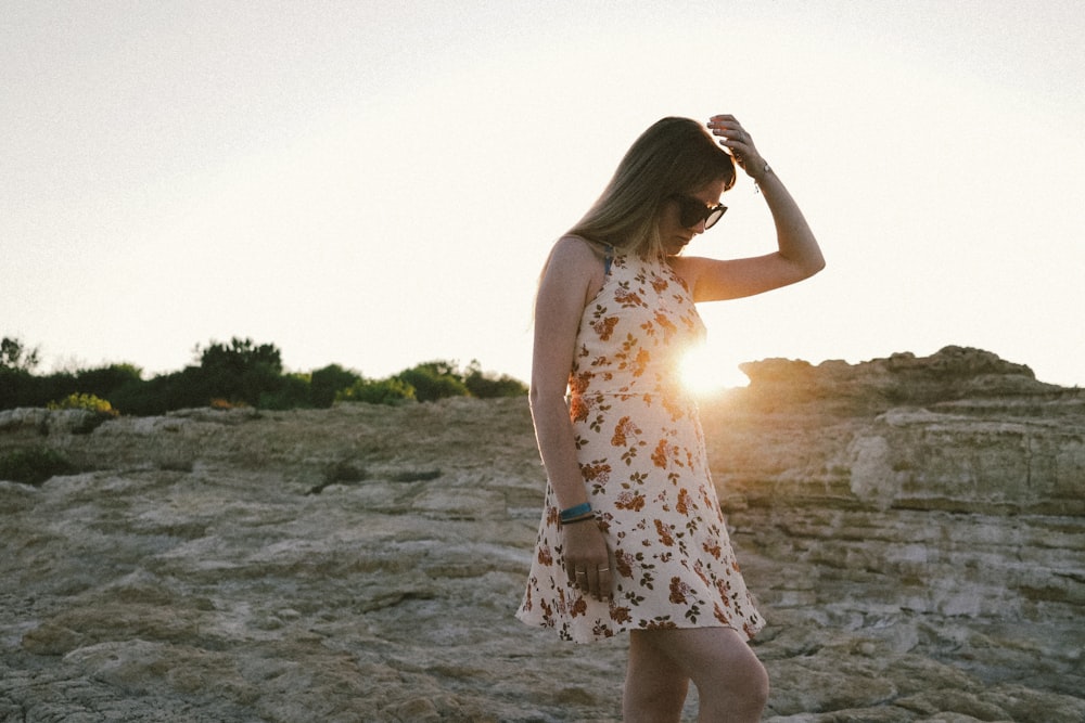 mujer en vestido floral blanco y rojo sin mangas de pie en la orilla del mar durante el día