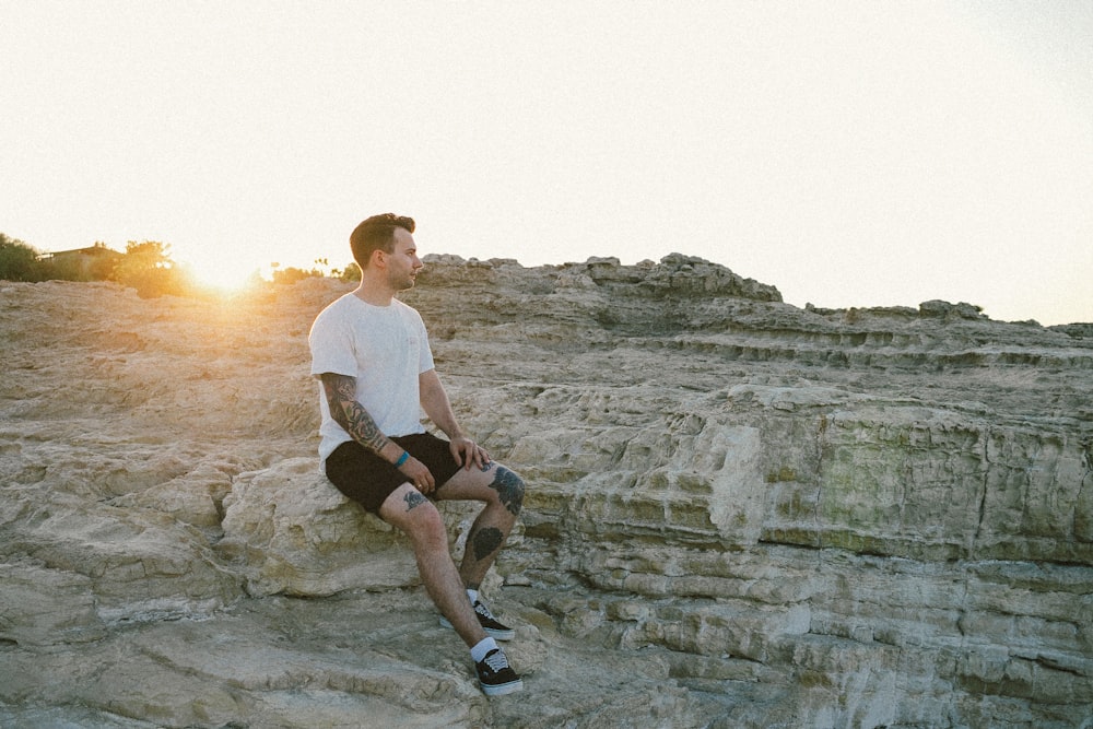 man in white t-shirt sitting on rock during daytime