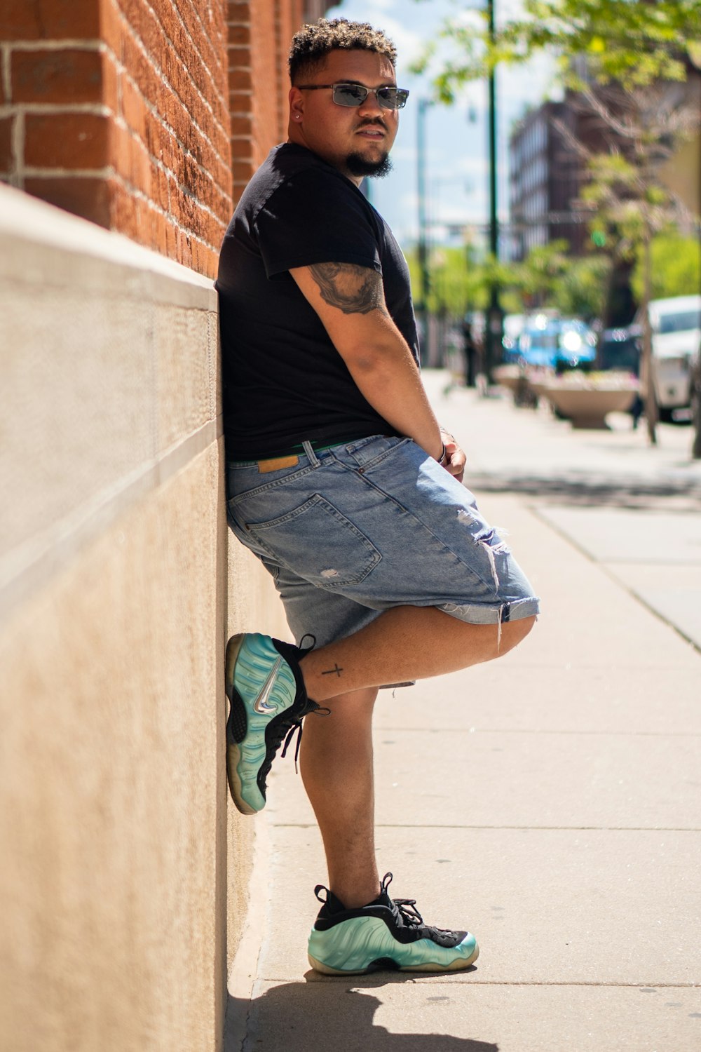 woman in black t-shirt and blue denim shorts leaning on wall during daytime