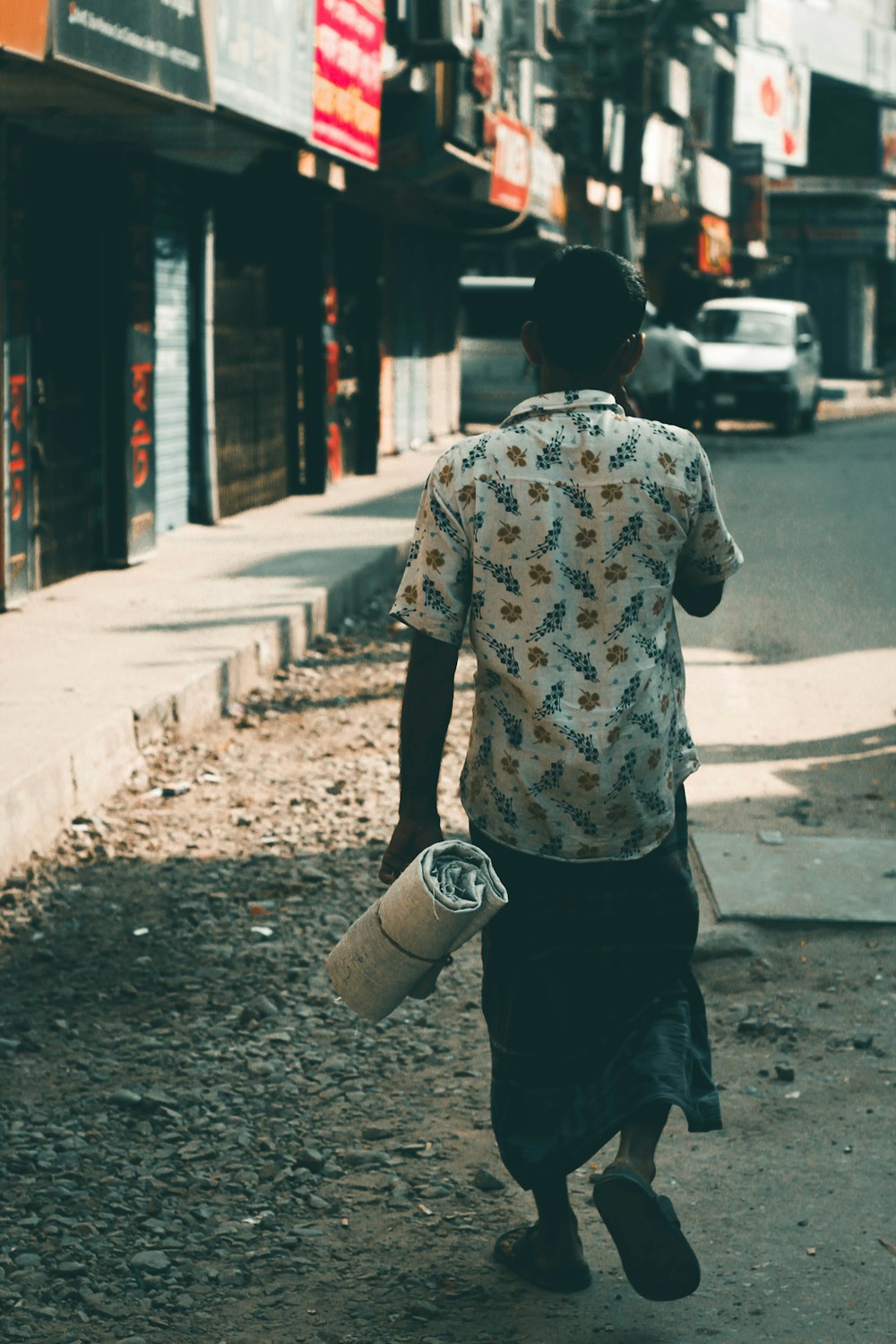 man in white and black floral shirt and black pants standing on sidewalk during daytime