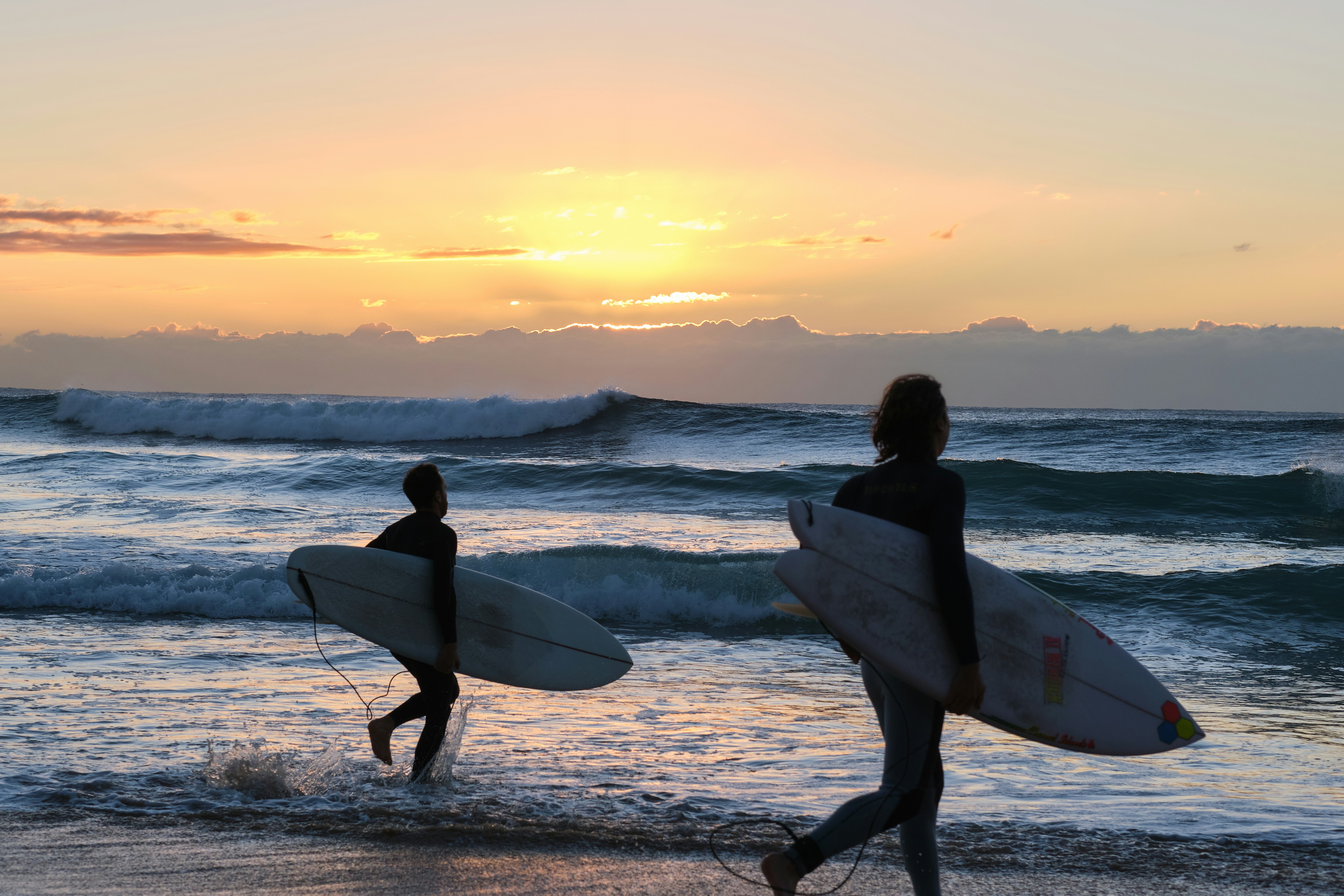 man holding white surfboard walking on beach during sunset