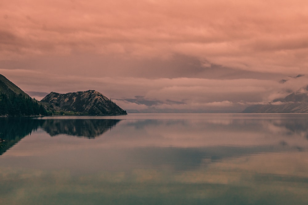 body of water near mountain under cloudy sky during daytime