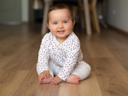 baby in white and black polka dot onesie crawling on brown wooden floor