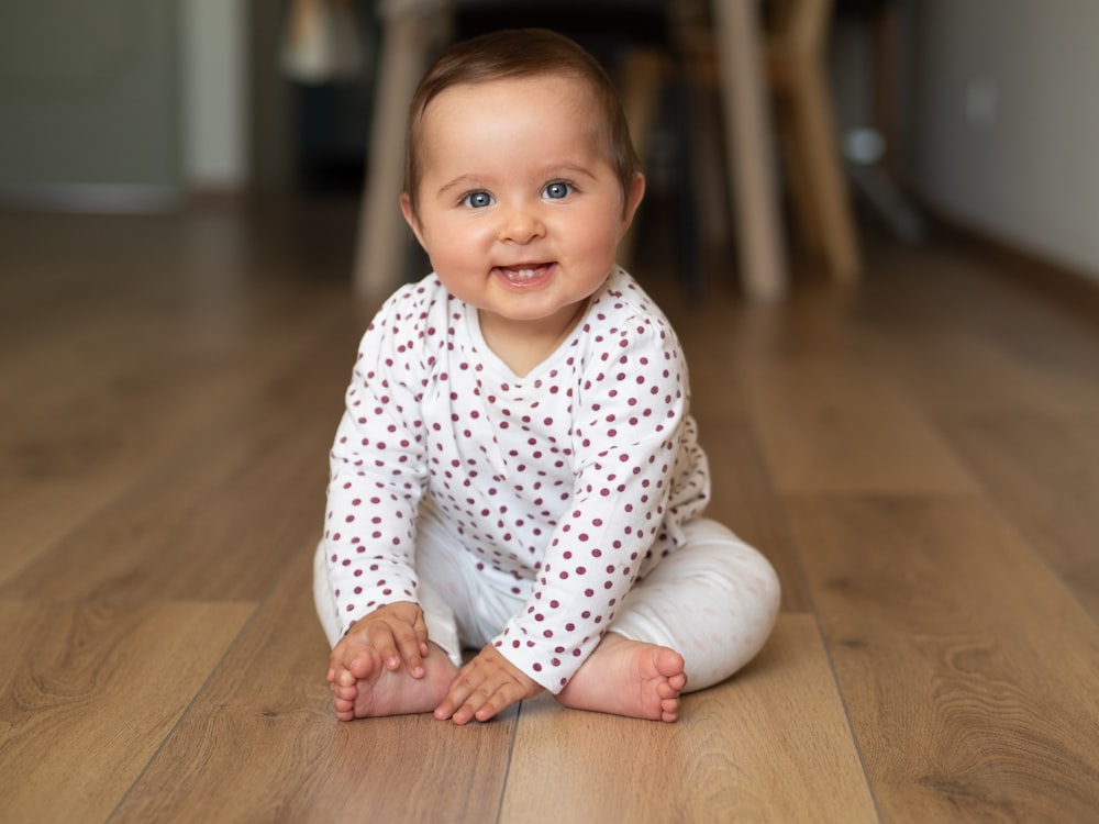 baby in white and black polka dot onesie crawling on brown wooden floor