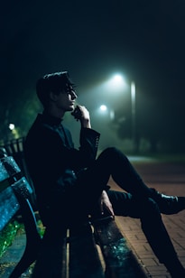man in black dress shirt sitting on bench during night time