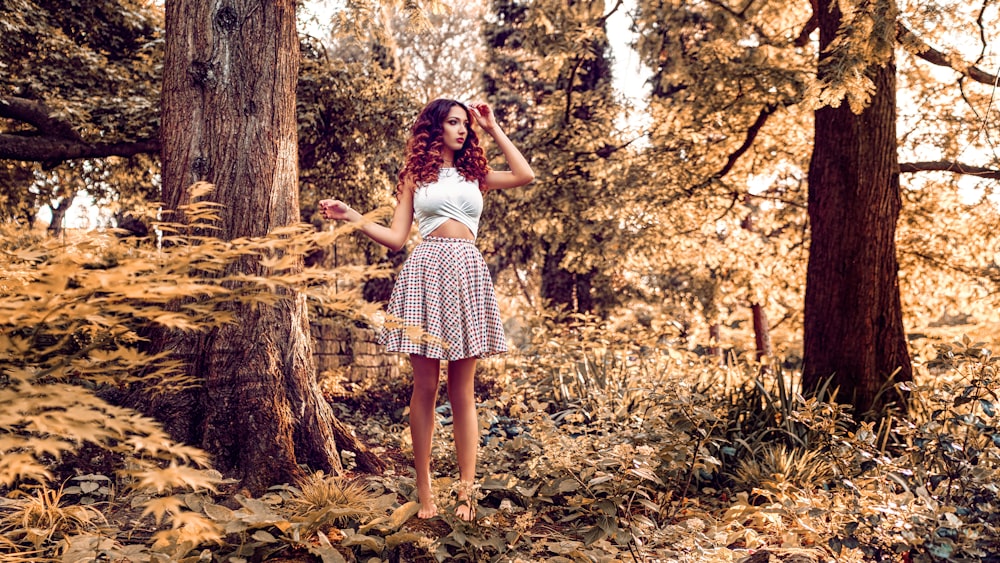 Femme en robe blanche debout sur des feuilles séchées brunes pendant la journée