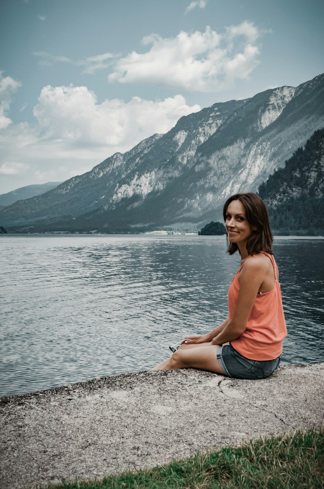 woman in pink tank top and blue denim shorts sitting on gray rock near body of near near near near