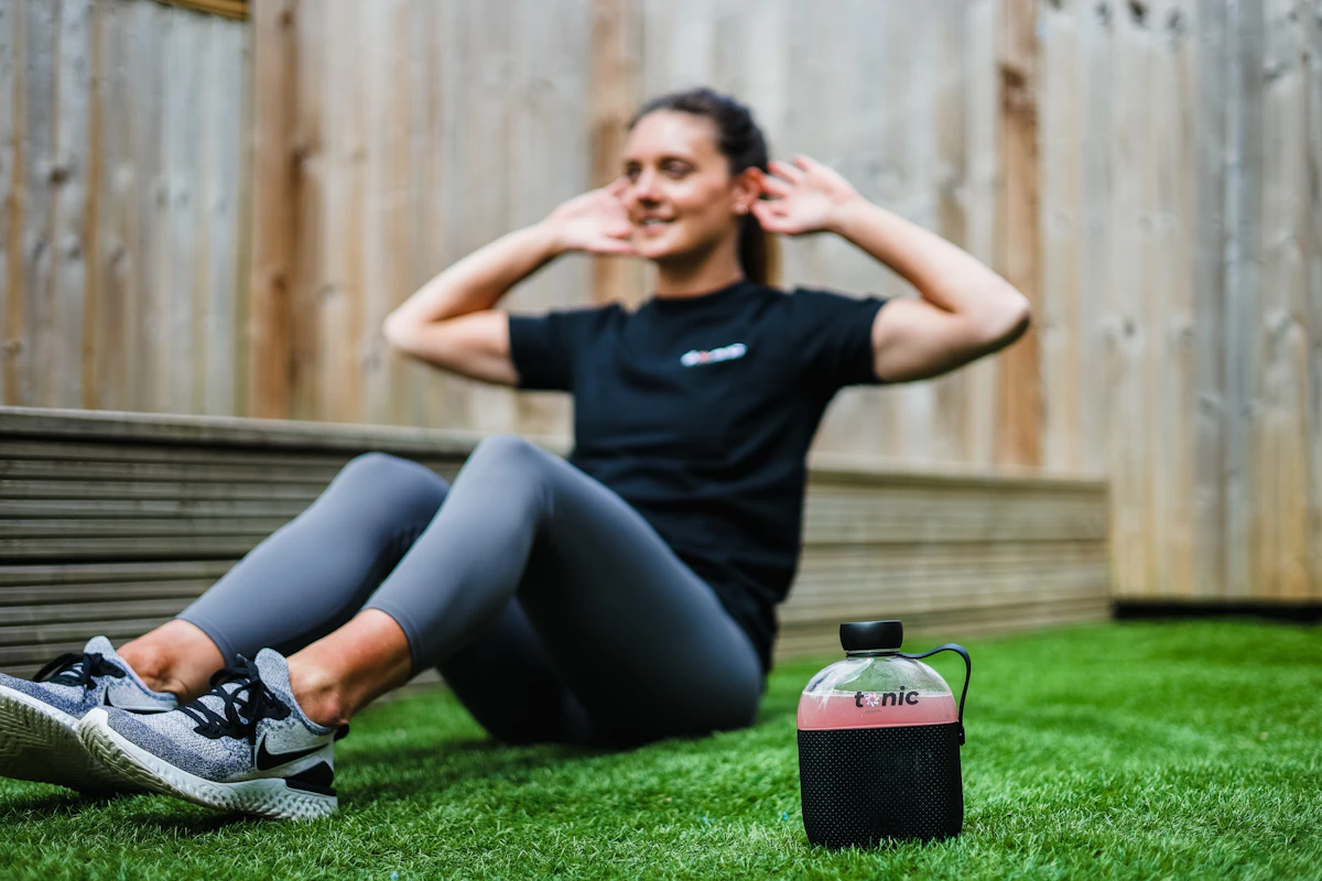 A woman doing sit-ups on the grass with a water bottle beside her