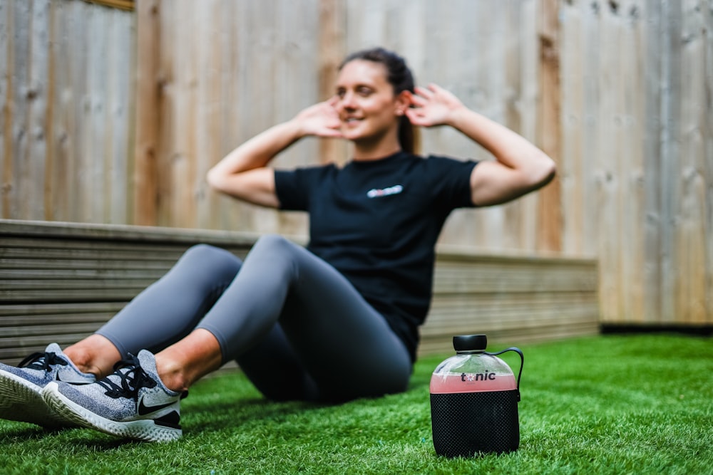 Femme en t-shirt à col rond noir et leggings noirs allongée sur un champ d’herbe verte