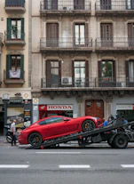 A professional driver carefully loading a luxury car onto a transport truck.