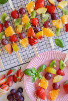 Brightly colored fruit skewers with strawberries, grapes, and melon cubes on a wooden table.