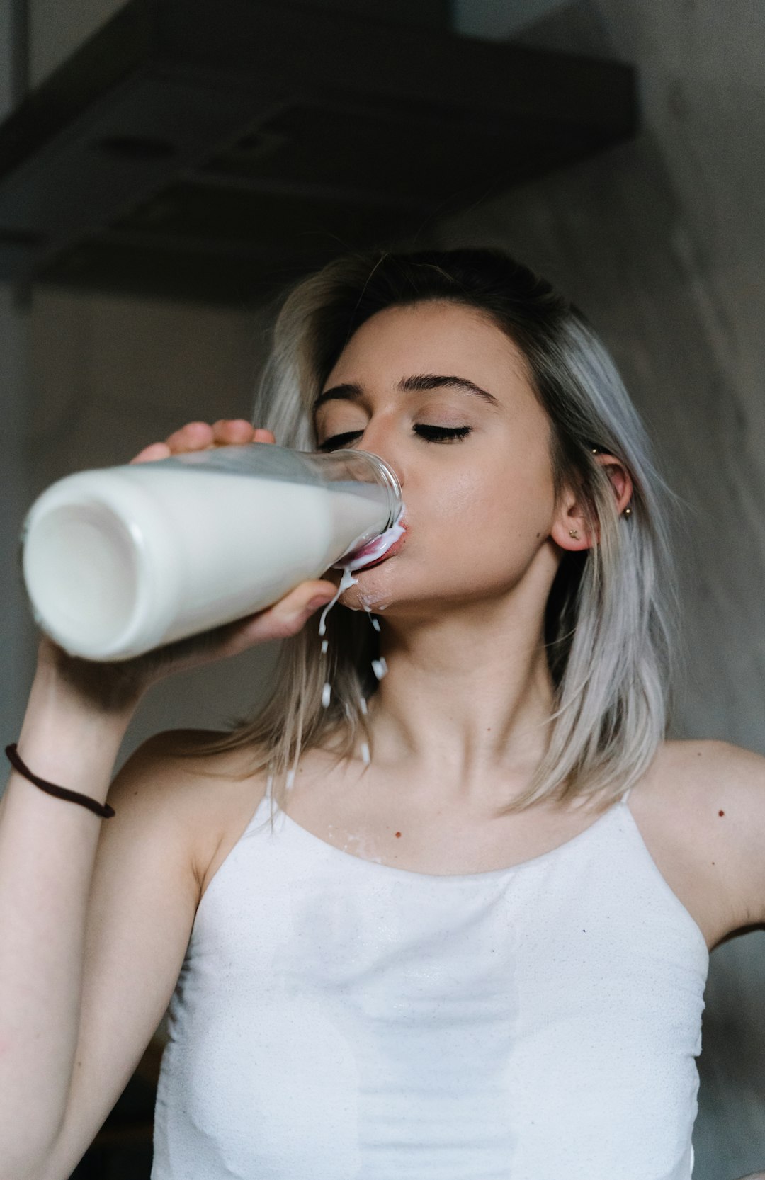 woman in white tank top drinking milk from clear drinking glass
