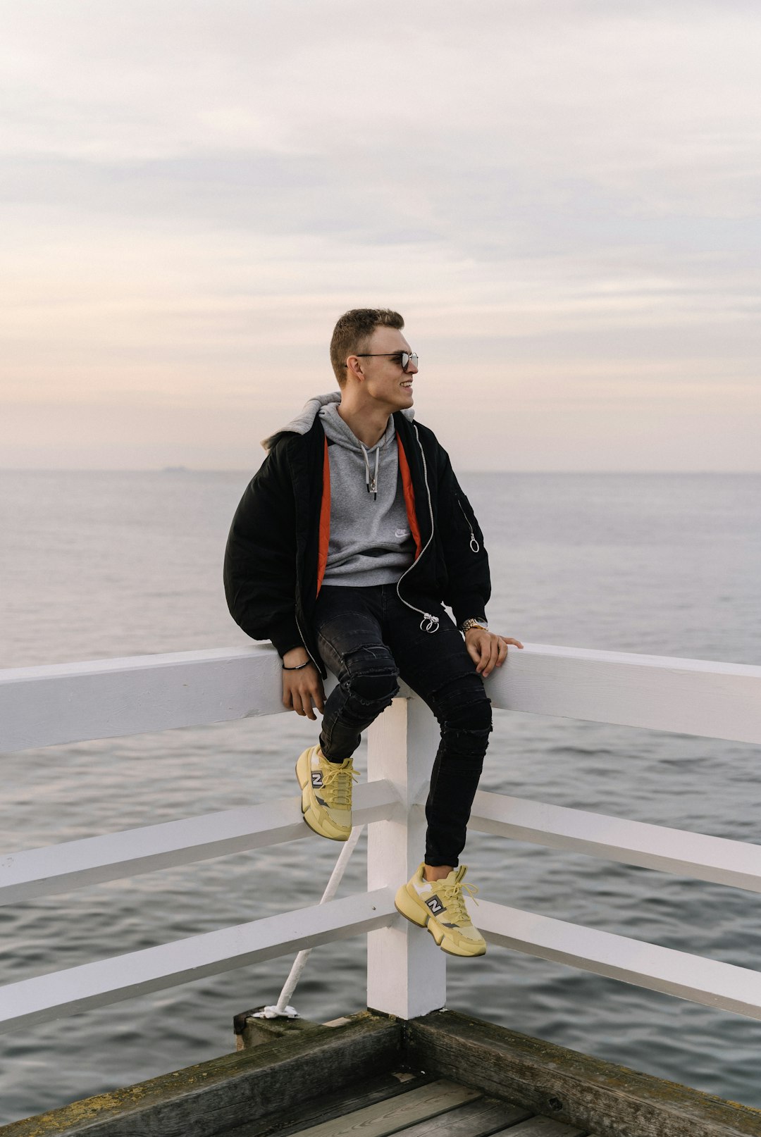 man in black jacket and black pants wearing yellow nike sneakers standing on gray sand during