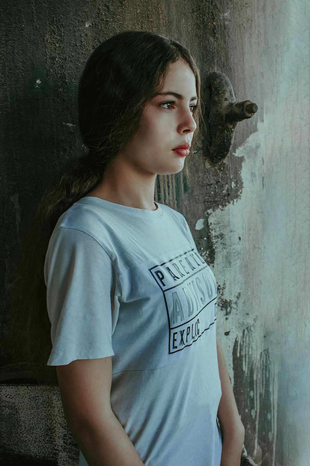 woman in gray crew neck t-shirt standing beside gray concrete wall