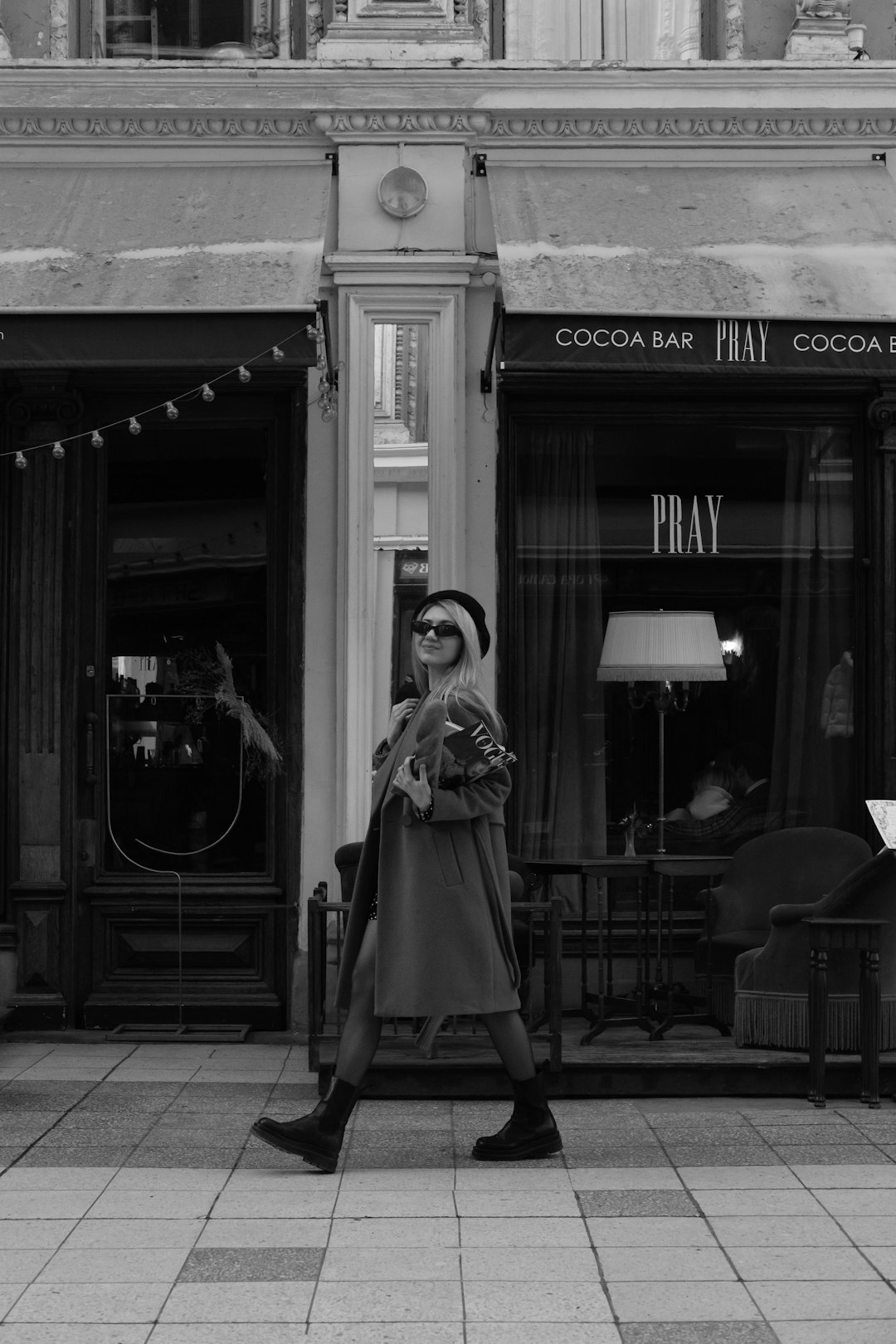 grayscale photo of woman in coat standing near building