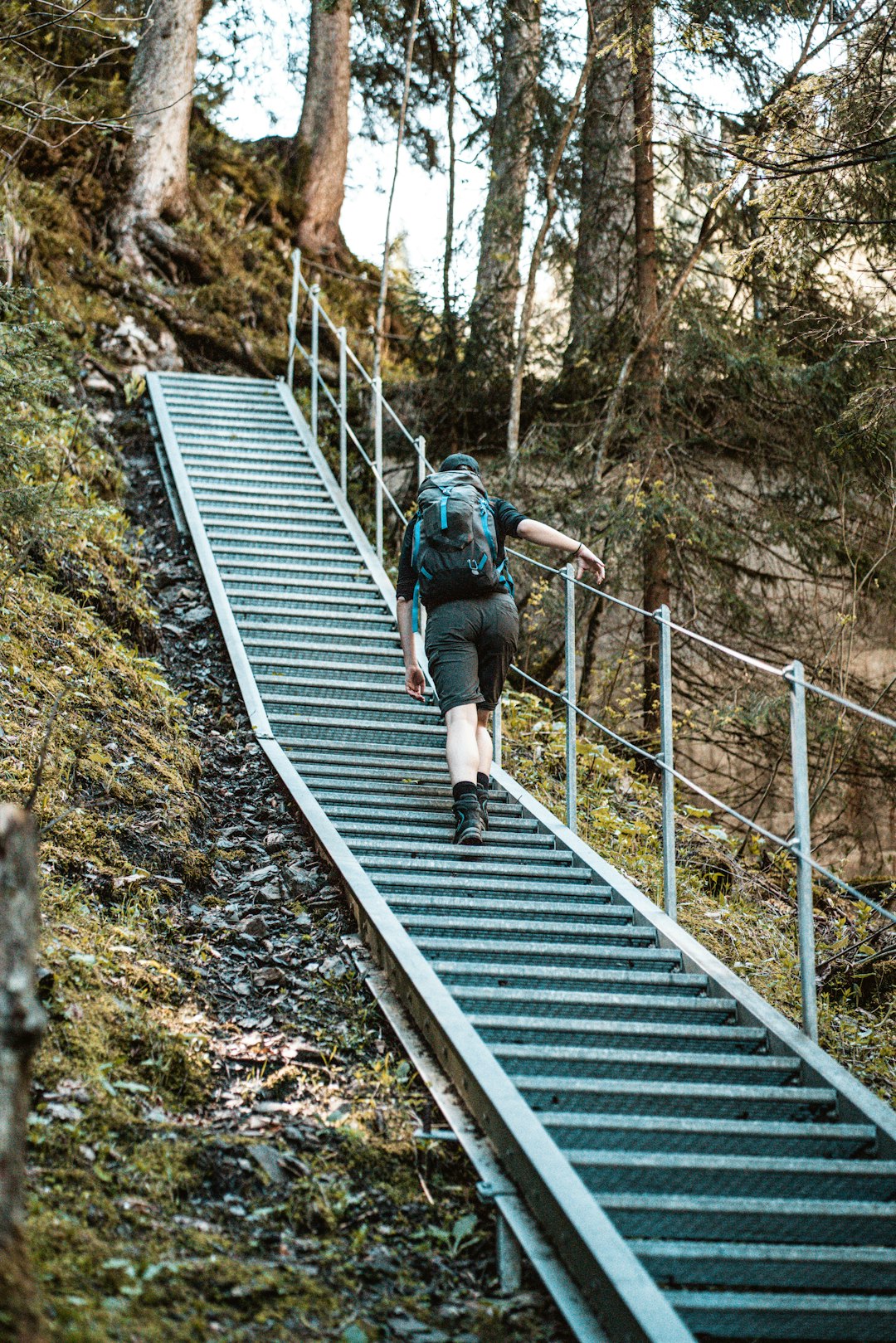 man in black jacket and blue denim jeans walking on gray metal bridge