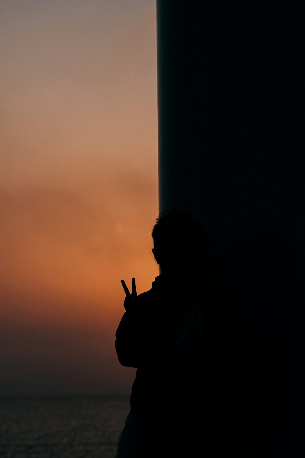 silueta de un hombre parado cerca de un poste blanco durante la puesta de sol