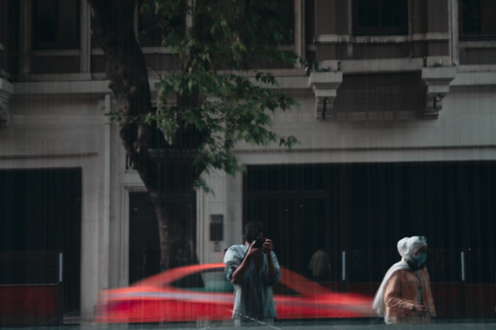 man in black jacket and white cap sitting on red car hood