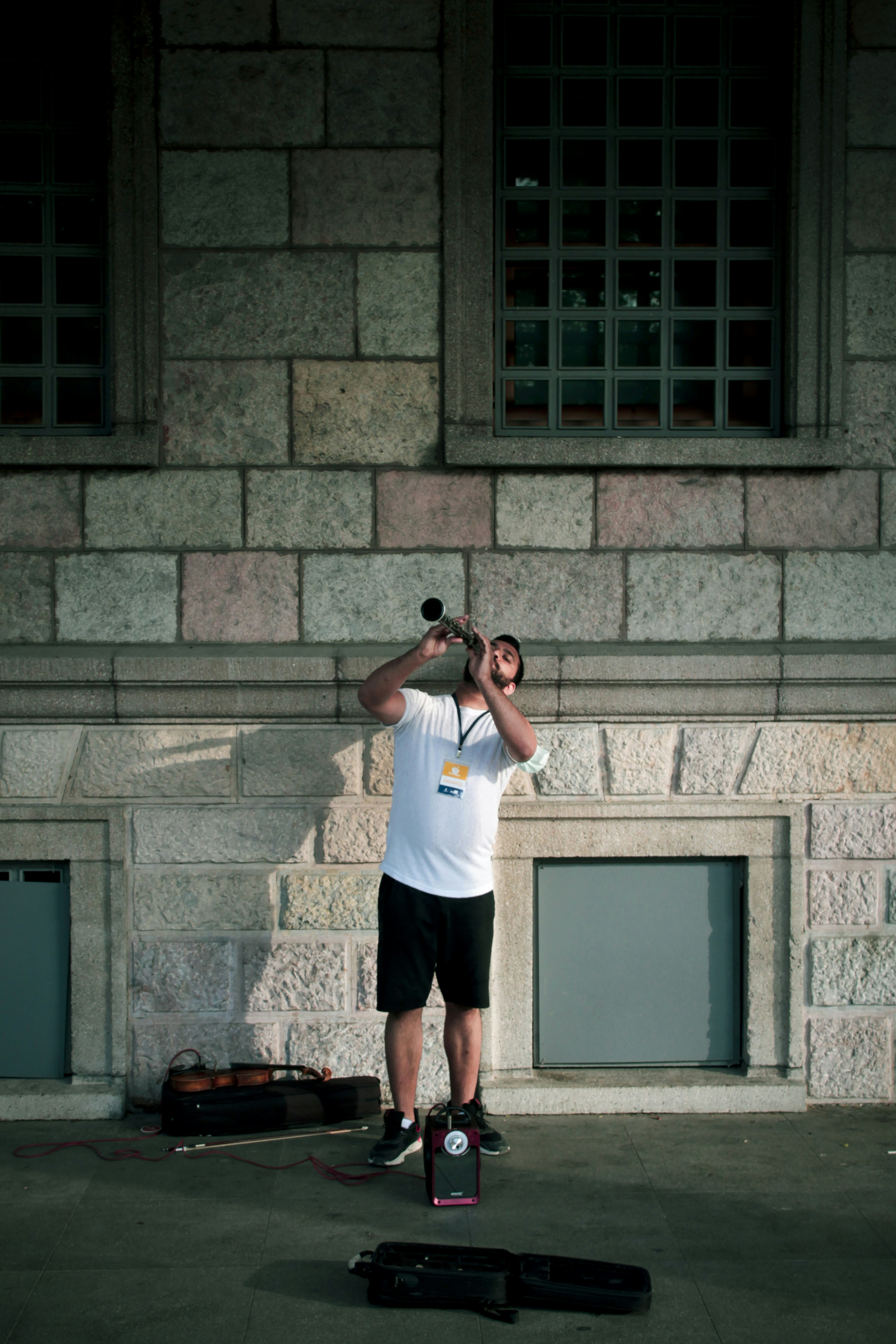 man in white t-shirt and black shorts standing beside brown brick wall during daytime