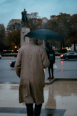 Model wearing an elegant beige trench coat walking through a softly lit urban street at dusk.