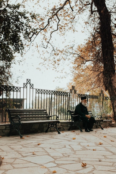 An elderly man sitting on a park bench, reflecting.