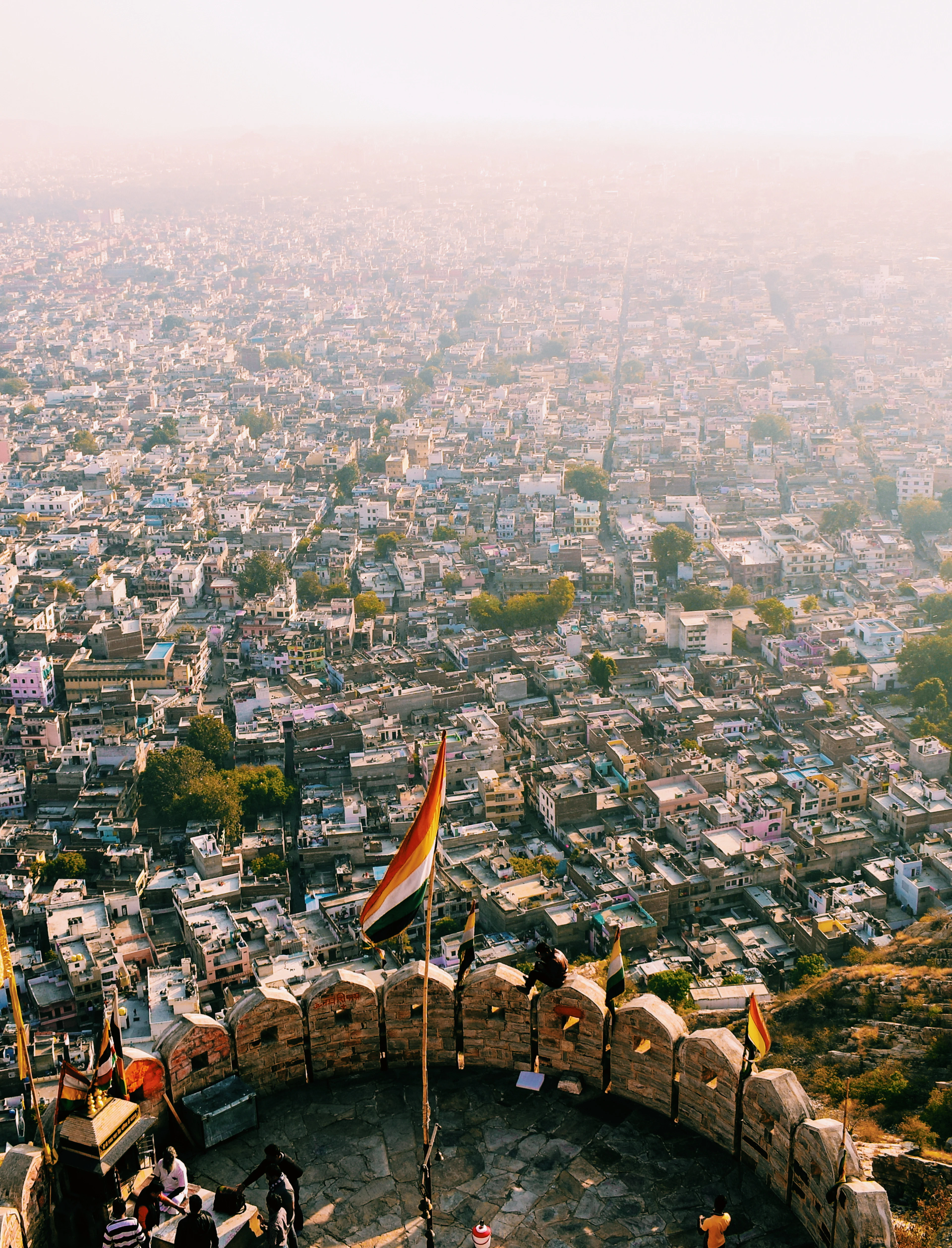 Jaipur's dense rooftops spread hazily to the horizon, seen from a hilltop fort's flag-topped rampart.