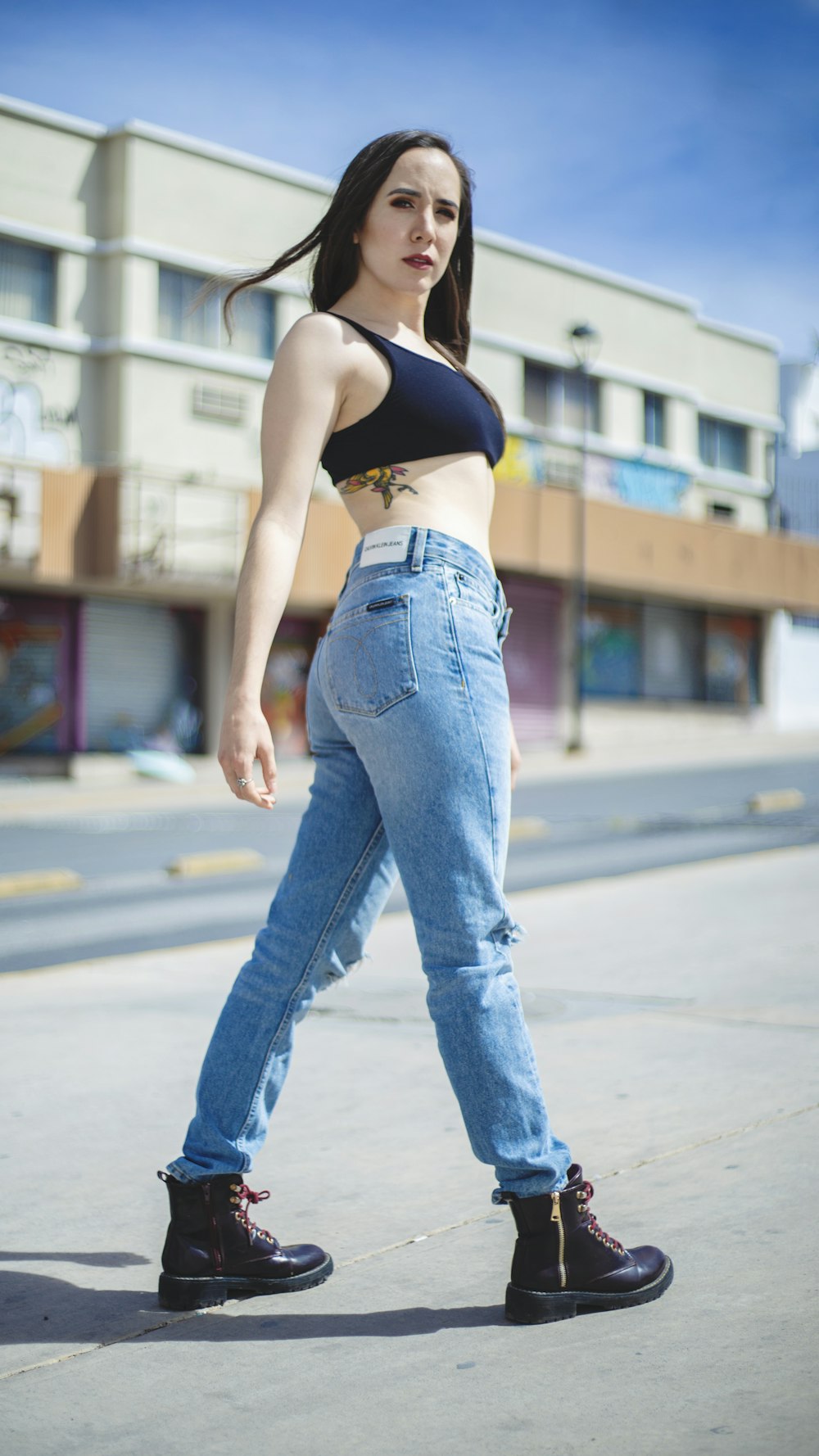 woman in blue denim jeans and black sports bra standing on road during daytime