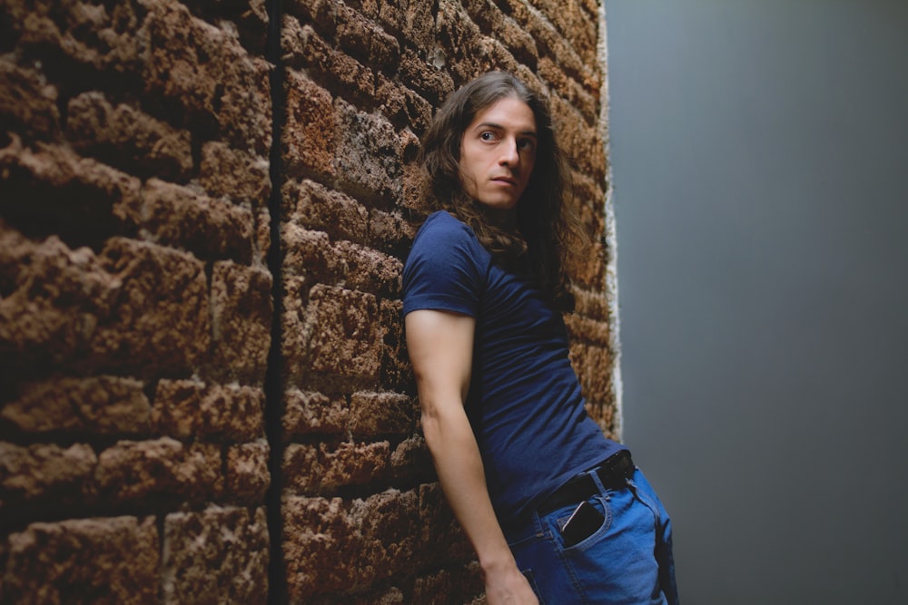 woman in black t-shirt and blue denim jeans leaning on brown concrete wall