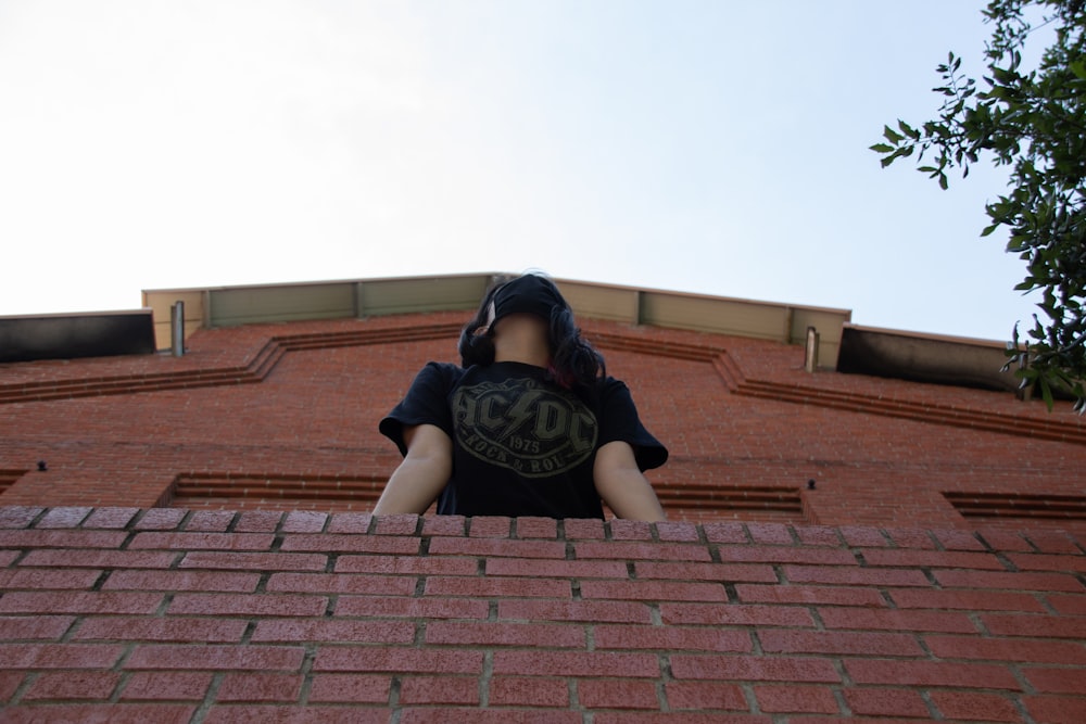 man in black t-shirt and black pants sitting on brown brick wall during daytime