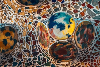 A vibrant mosaic artwork featuring circular patterns in various colors, including blue, yellow, and green. The background consists of irregularly shaped, colorful shards creating a complex and dynamic pattern.