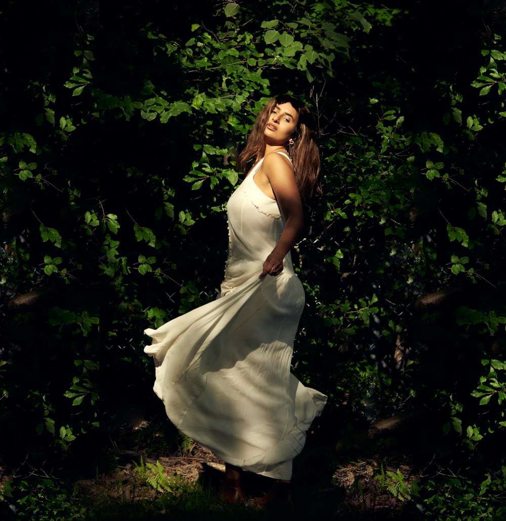 woman in white spaghetti strap dress standing on green grass field during daytime