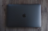 A closed, space gray laptop with a prominent black apple logo on the center of the top cover rests on a wooden surface.