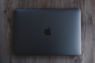 A closed, space gray laptop with a prominent black apple logo on the center of the top cover rests on a wooden surface.